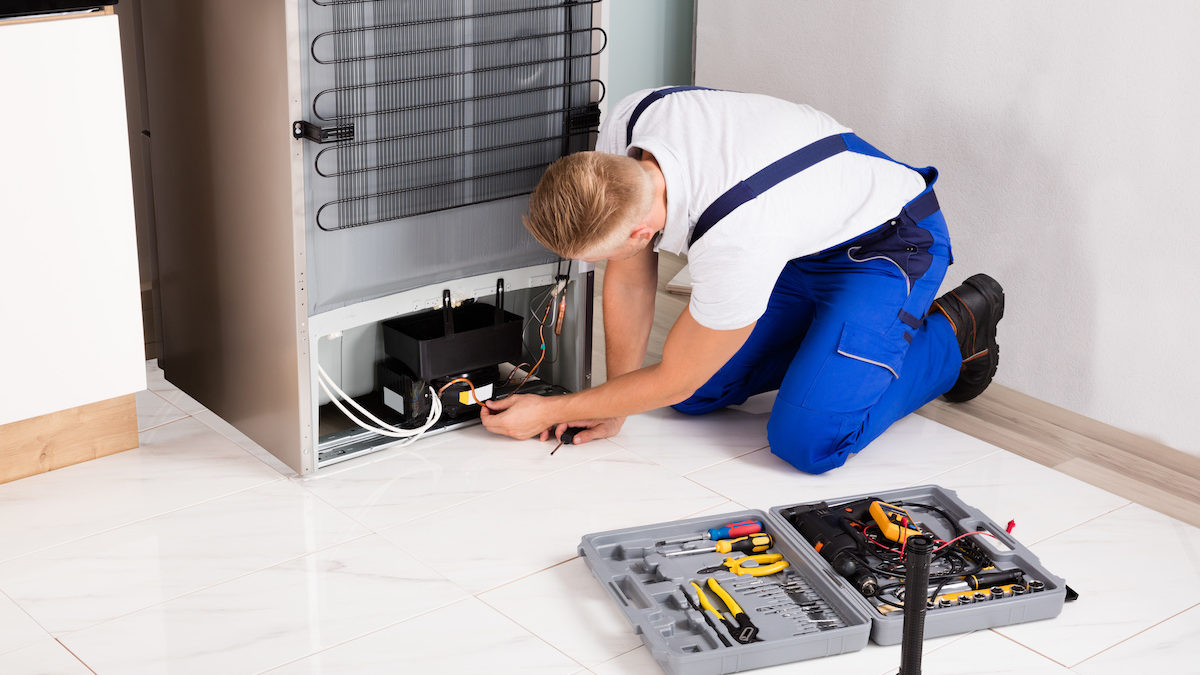 Young Male Technician Checking Refrigerator With Screwdriver