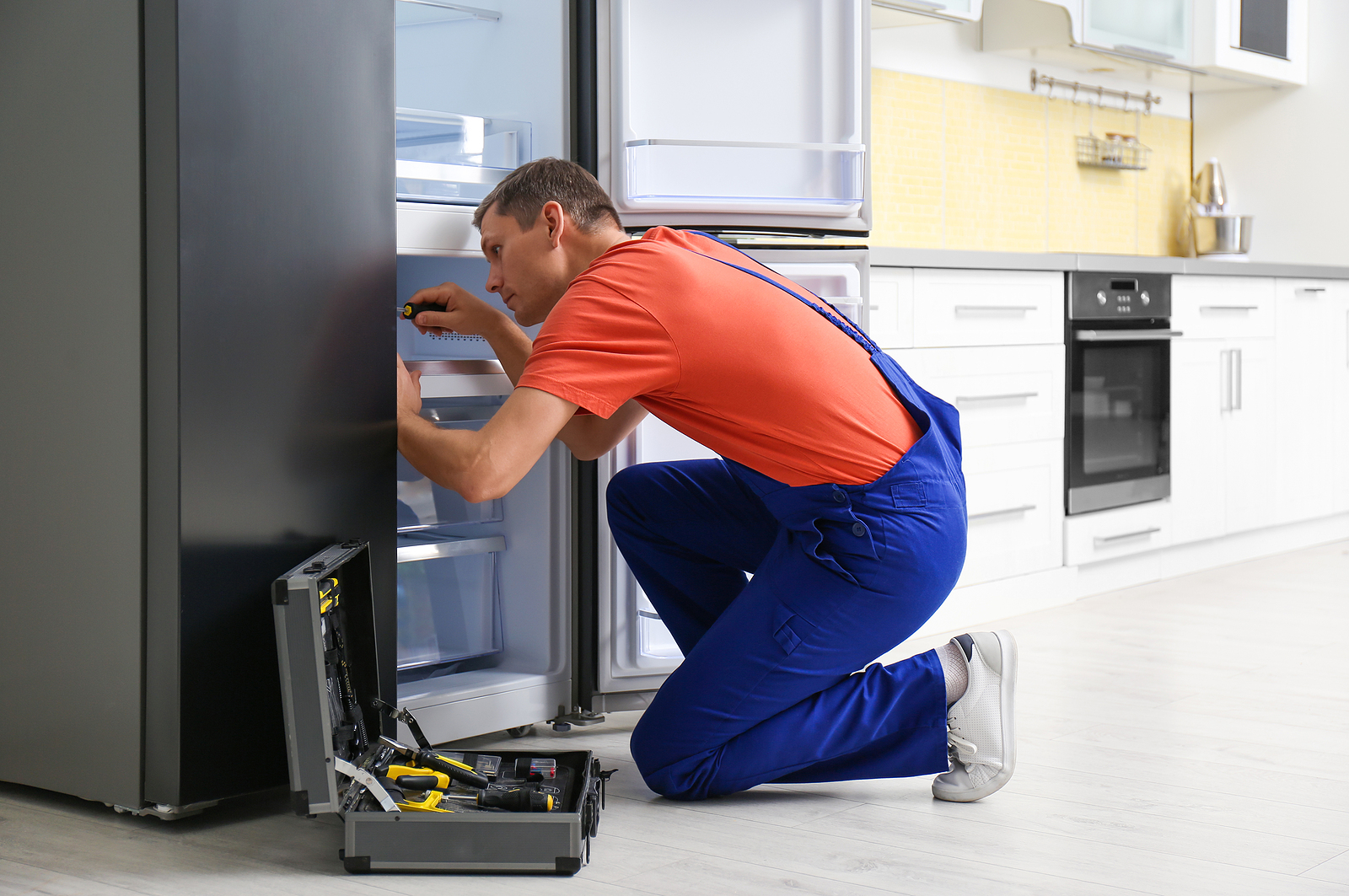 Male technician with screwdriver repairing refrigerator in kitchen